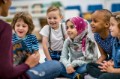 A multi-ethnic group of young school children are indoors in their classroom. Their teacher is reading a storybook to them.